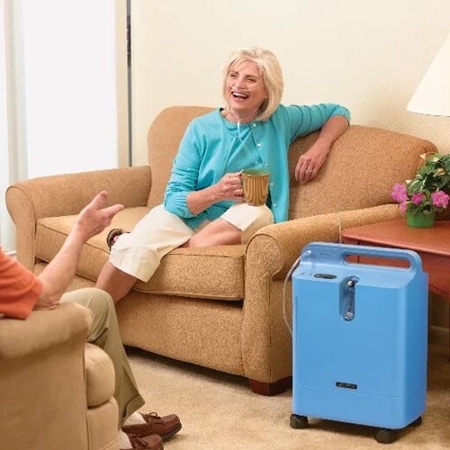 Woman relaxing on a sofa at home beside a Philips EverFlo oxygen concentrator